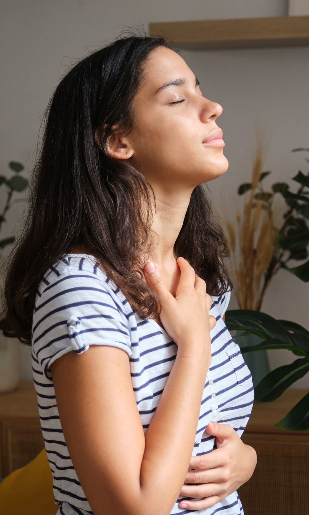 mujer respirando profundamente en casa, rodeada de plantas