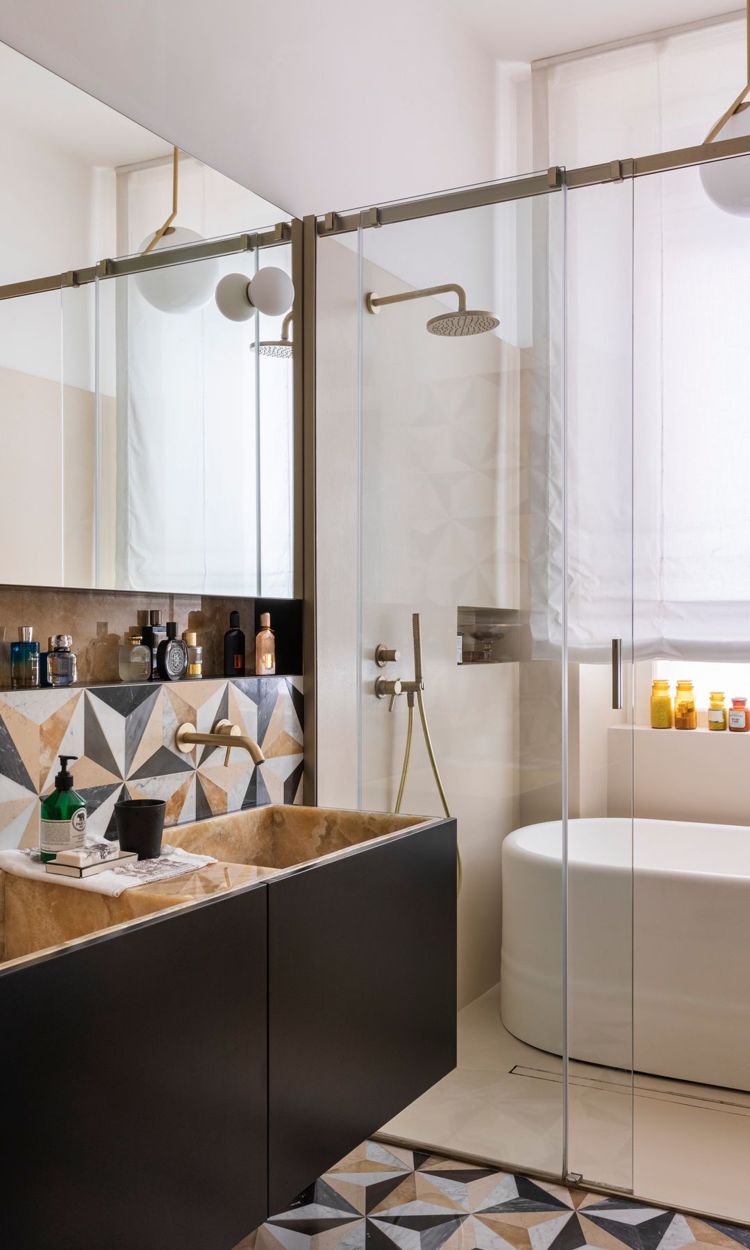 Baño con bañera y ducha, separados del lavamanos mediante una corredera de cristal, revestimiento de azulejos geométricos, mueble lavabo de madera oscura con lavamanos de piedra, estor blanco