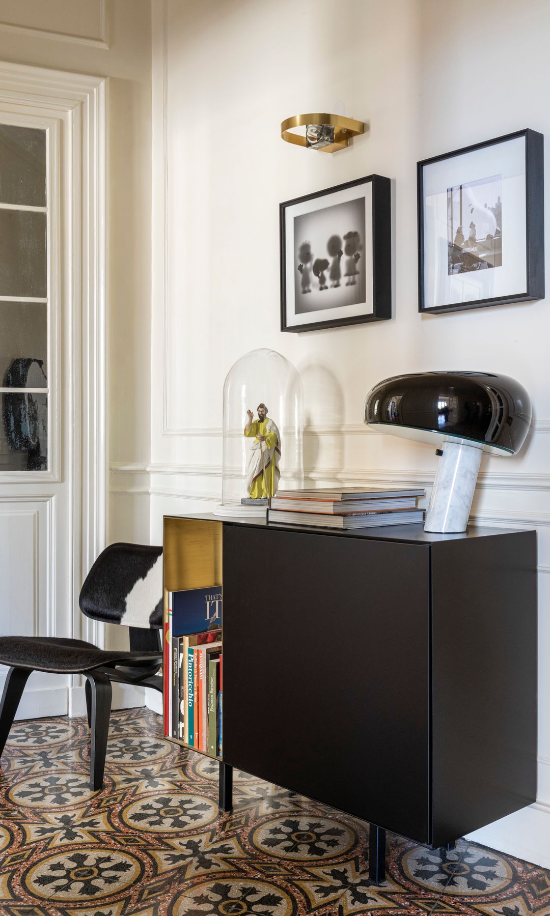 Rincón con mueble negro, lámpara seta, cuadros, silla, adornos, suelo hidráulico