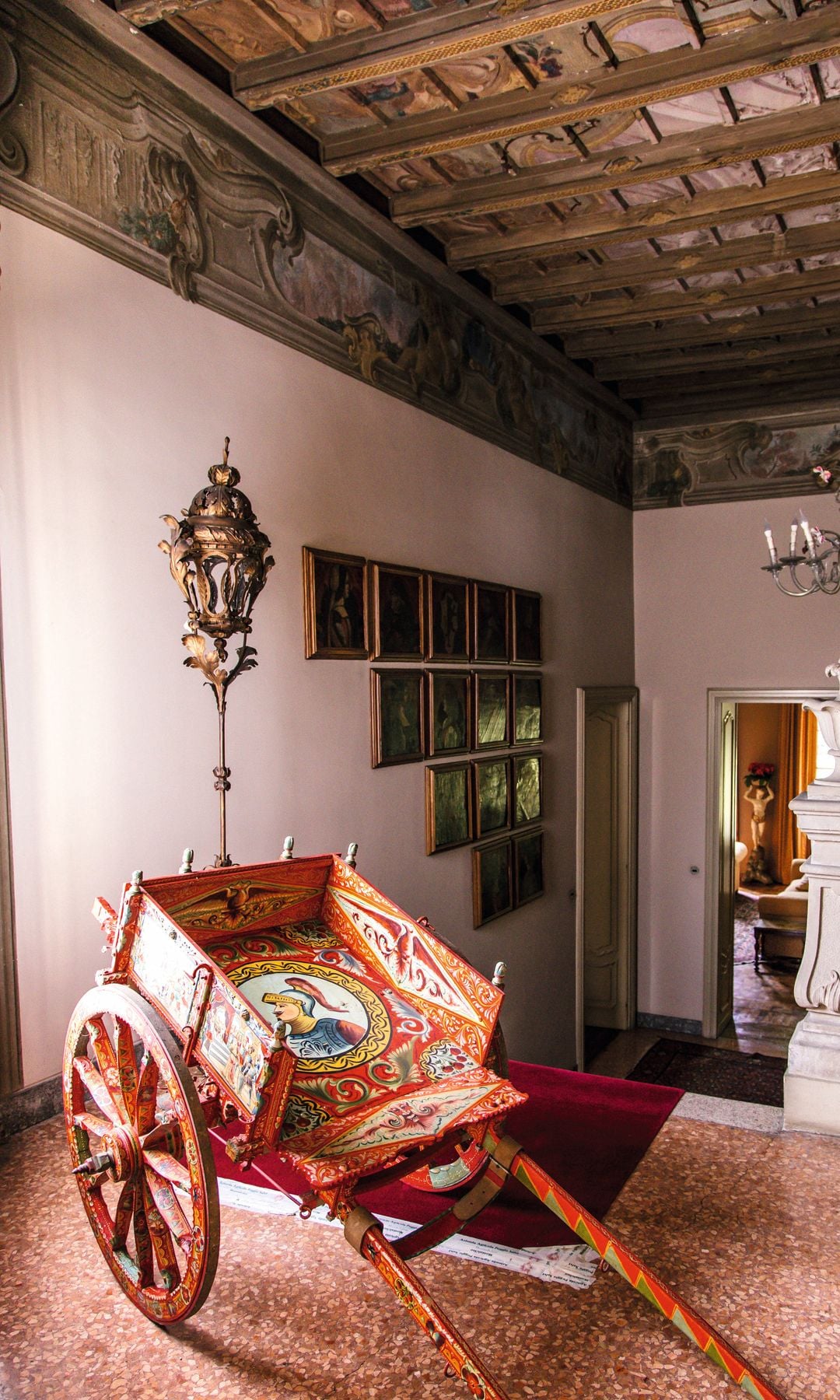 Una imagen del interior, donde descansa un típico carro siciliano. En la otra página, arriba, el dormitorio principal de la casa, con cabecero con cama en madera y metal de estilo floral, del siglo XVIII. La lámpara es de cristal de Murano y las paredes están decoradas con imágenes religiosas. Abajo, el cuarto de baño del dormitorio, con bañera exenta de época