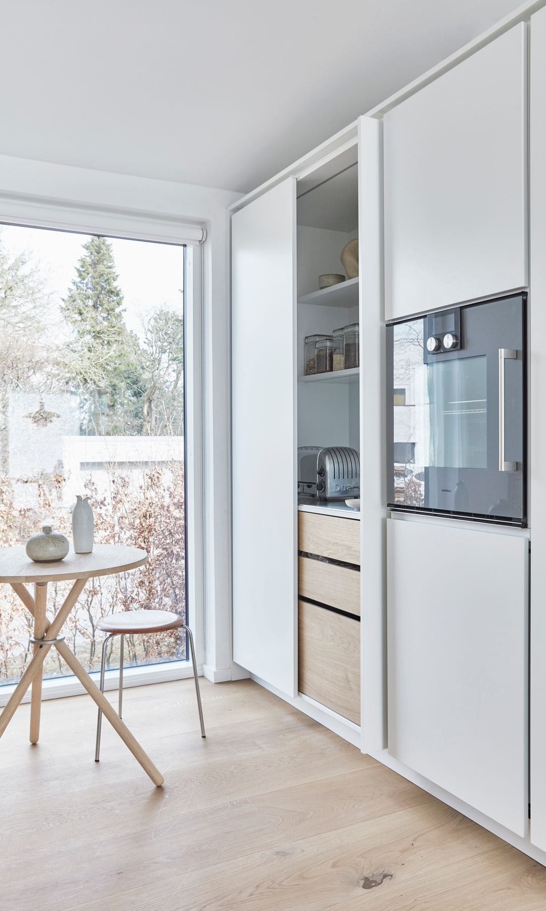 Cocina en un armario blanco con mesa de office redonda de madera, ventana