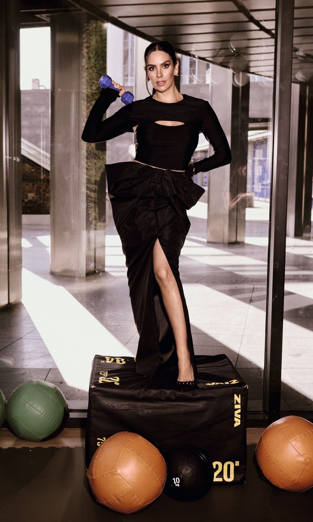 Cristina Pedroche en un atuendo negro, sosteniendo una mancuerna azul, posa sobre una caja de pesas.