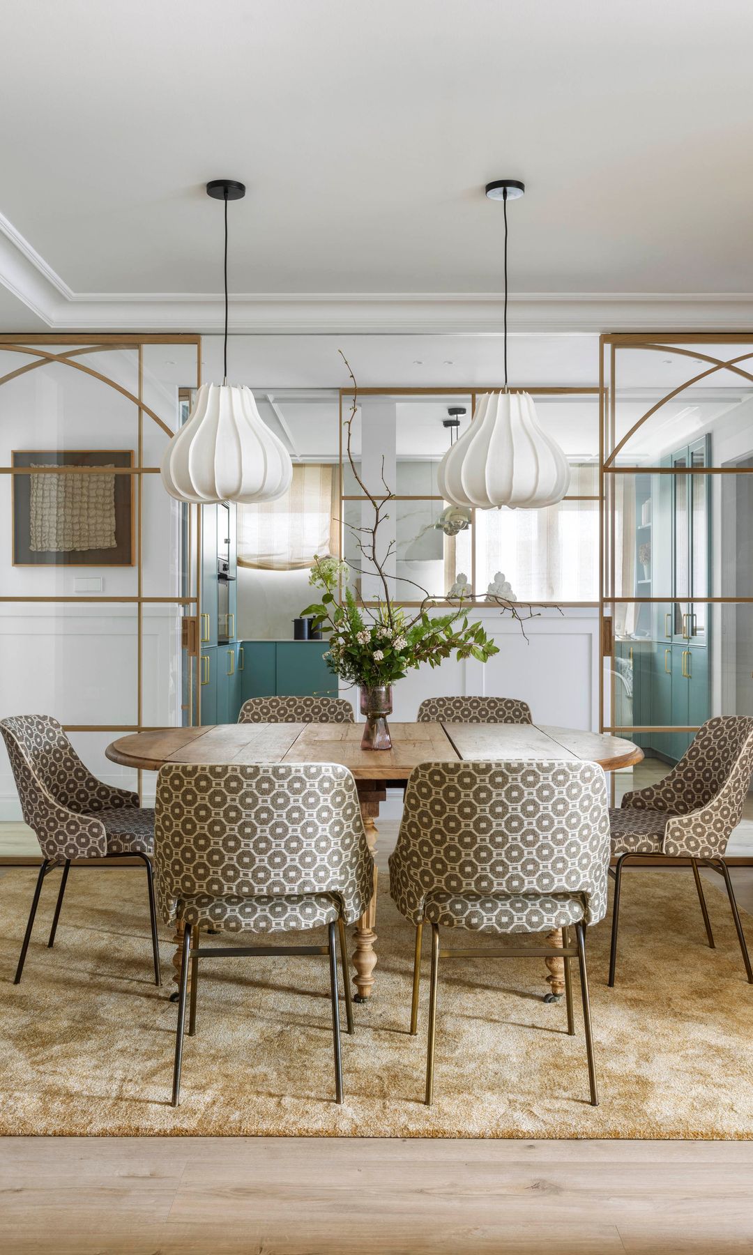 Comedor con mesas de madera, sillas tapizadas, alfombra dorada, lámparas de techo, puertas correderas con los marcos dorados, que separan el comedor de la cocina 