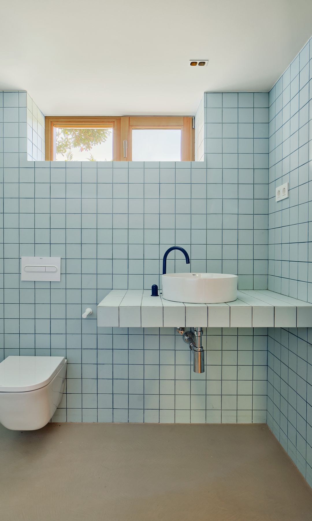 Baño revestido de azulejos azules, lavabo exento, grifo negro, sanitario suspendido 
