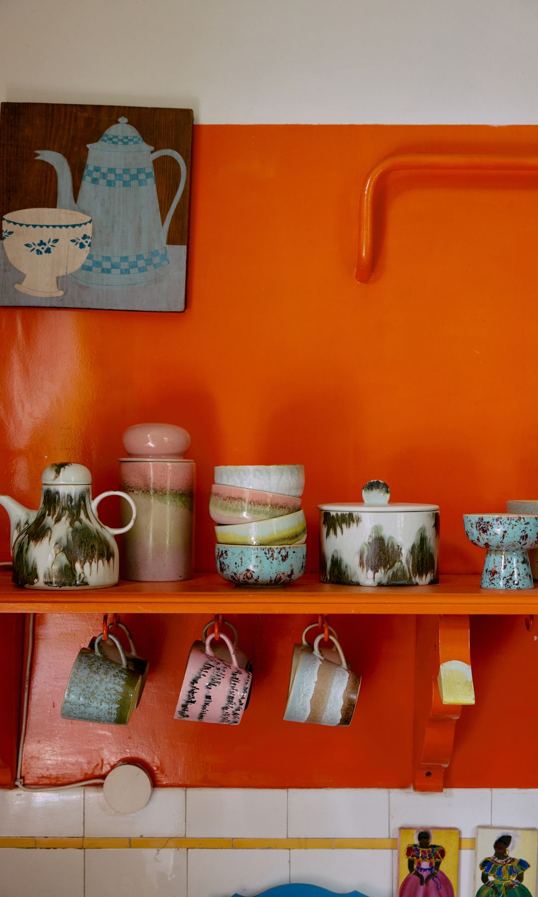 Cocina con pared naranja, balda naranja, tazas sobre la balda y en ganchos, antepecho de azulejos blancos