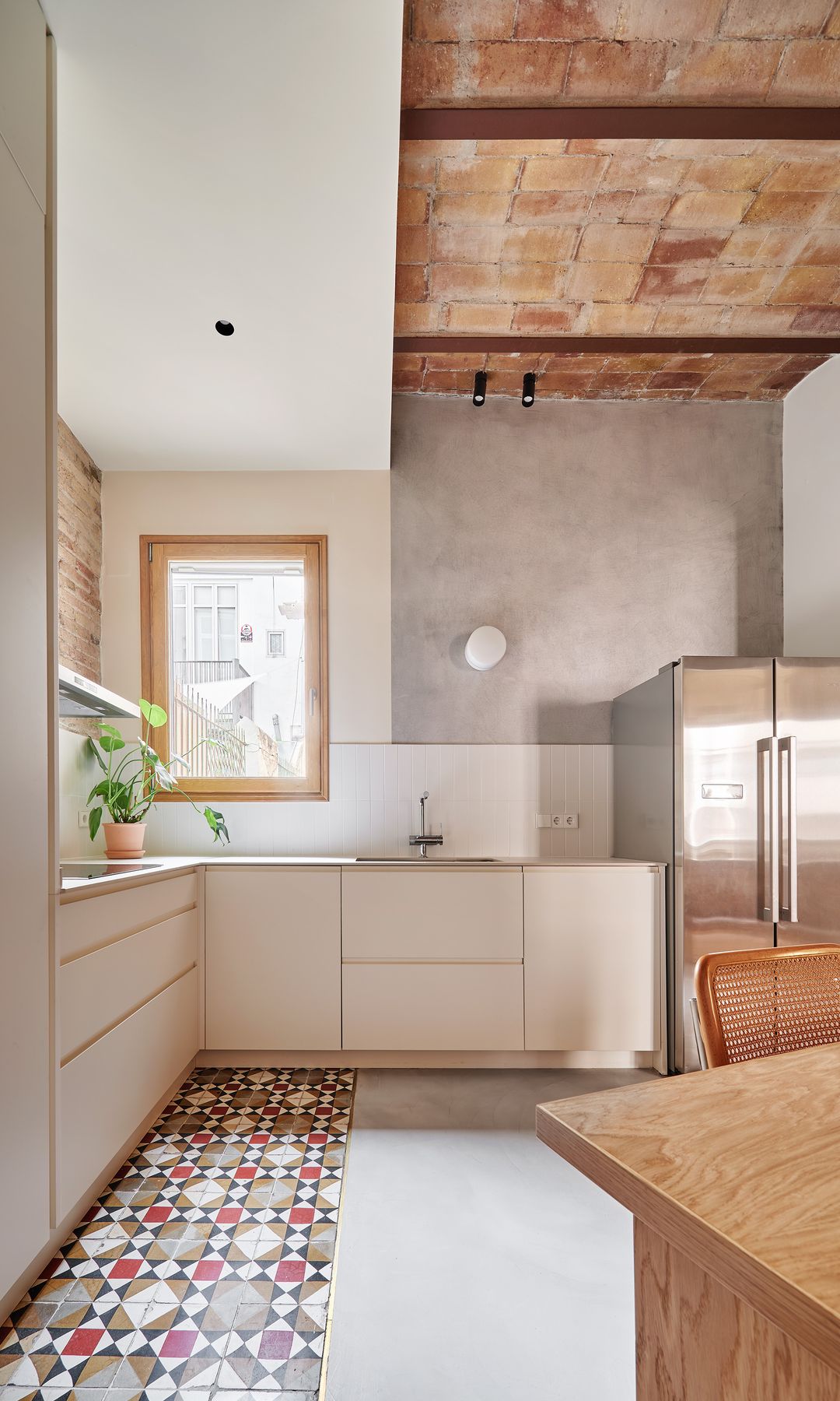 Cocina blanca con ventana, suelo hidráulico, bóvedas catalanas, ventana con el marco de madera, frigorífico doble de acero