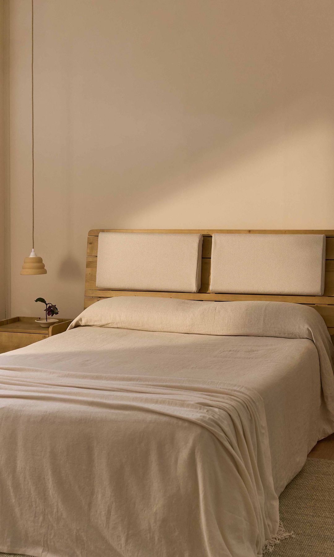 Dormitorio con cabecero de madera con almohadones en el cabecero, lámparas de techo a ambos lados, ropa de cama blanca, alfombra de fibras vegetales, mesitas de noche de madera