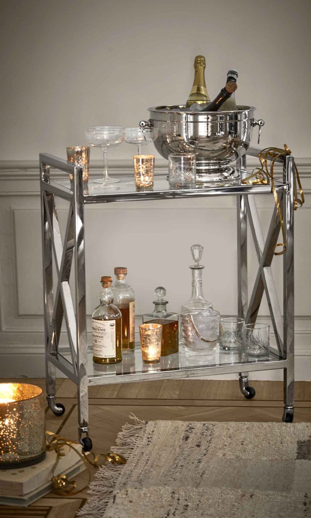 Carrito auxiliar metálico con bebidas, champanera, copas, botellas, vela en el suelo
