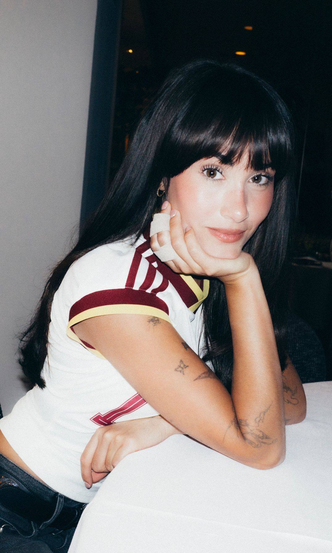 Aitana con melena larga oscura y flequillo abierto posa sentada en una mesa