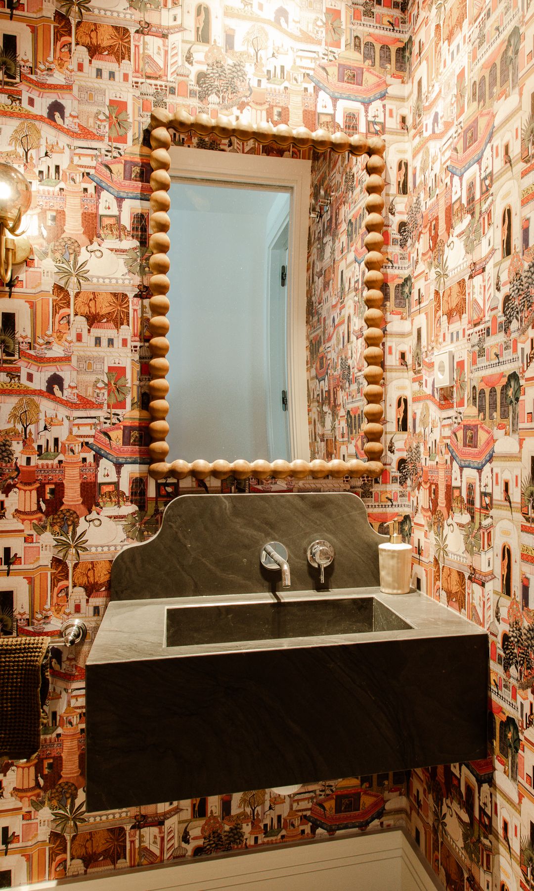 Aseo de cortesía con papel pintado de colores, lavabo negro y grifería empotrada espejo con marco de madera trabajado, aplique de pared