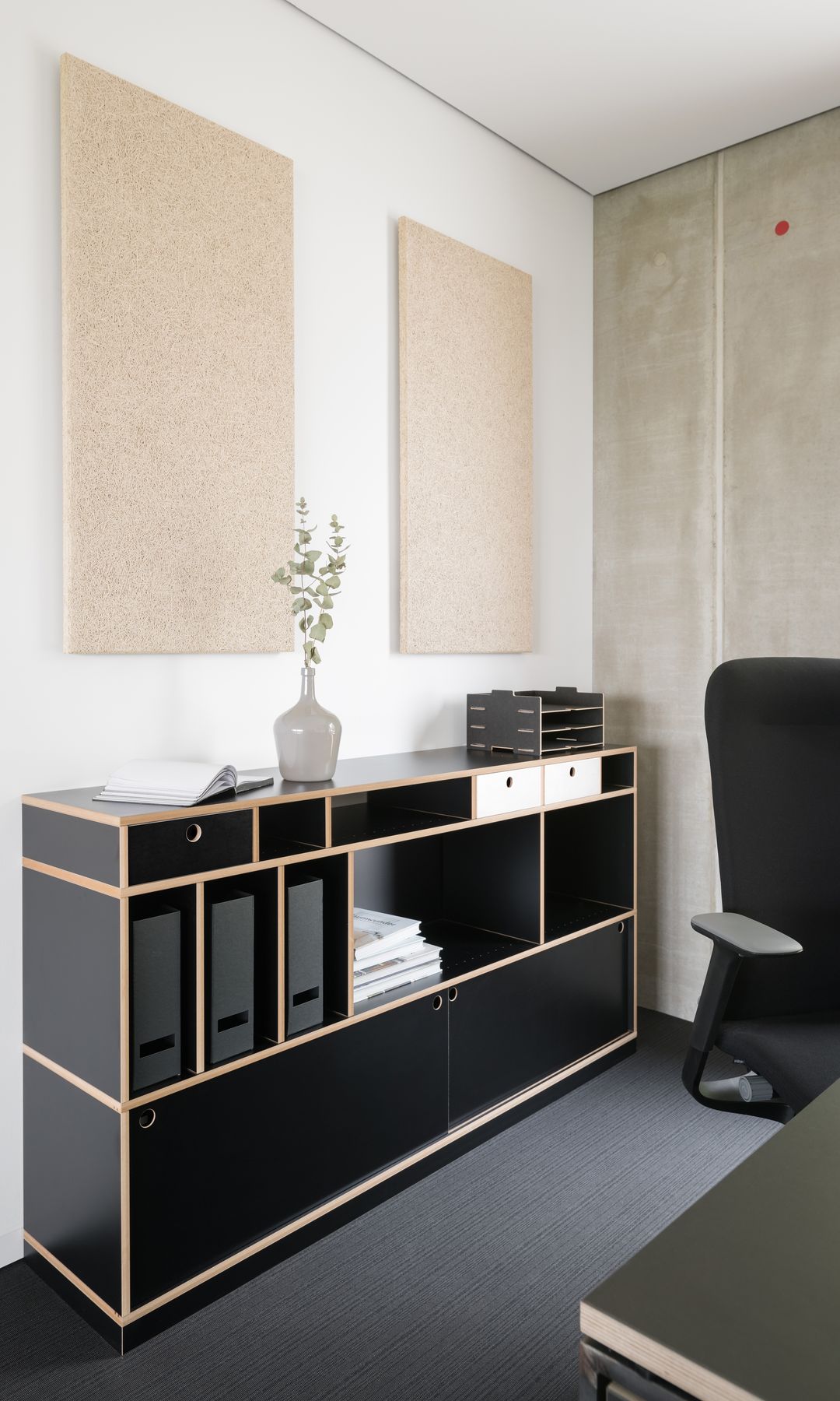 Despacho con mueble negro con cajones y compartimentos, cuadros en la pared, silla de oficina 
