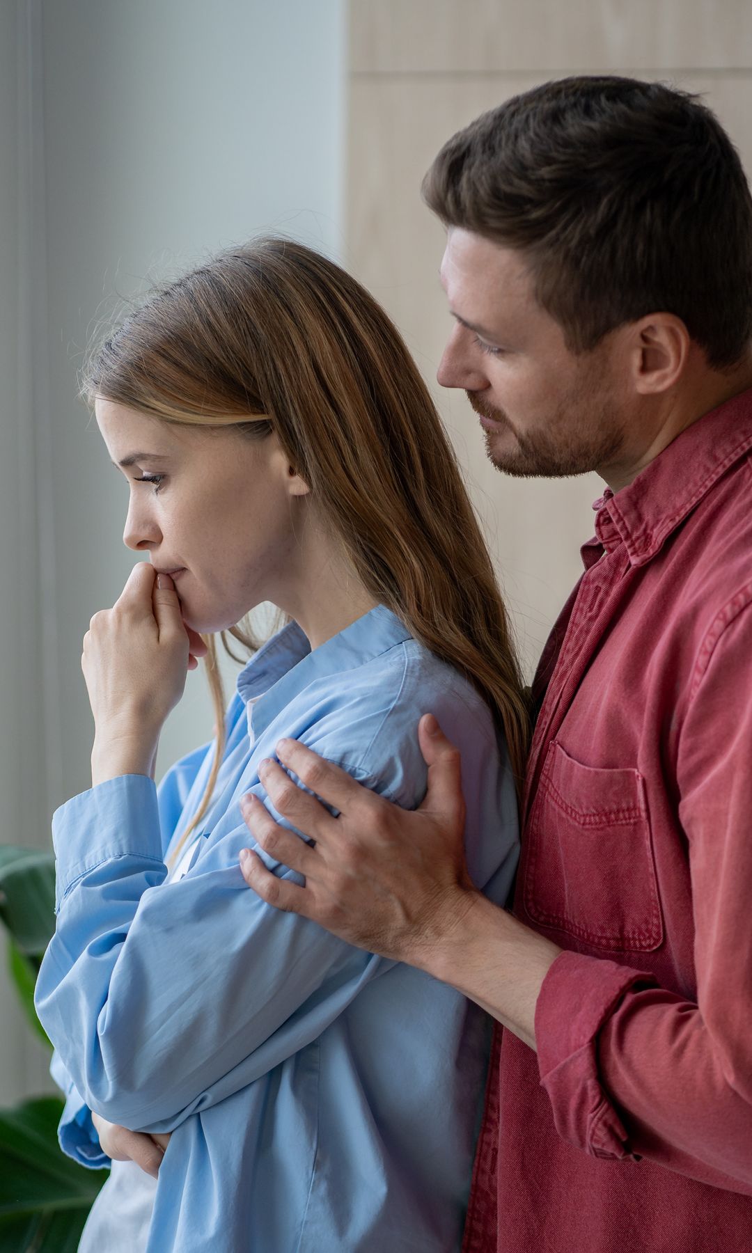 pareja consolando a su mujer, junto a la ventana de su casa