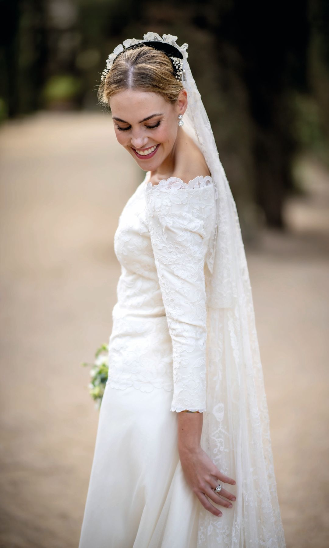 Eugenia en traje blanco con velo largo, sonriendo en un entorno natural.