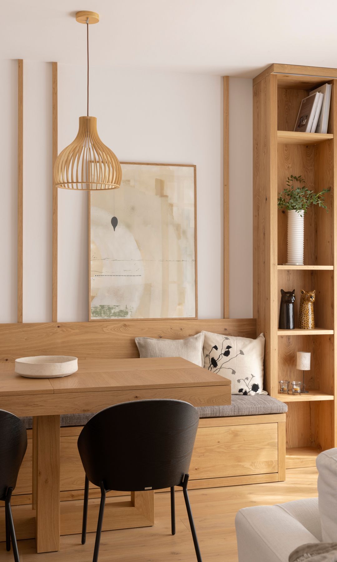 Office con banco de madera, estantería de madera, mesa de madera, sillas negras, lámpara de techo de fibras vegetales