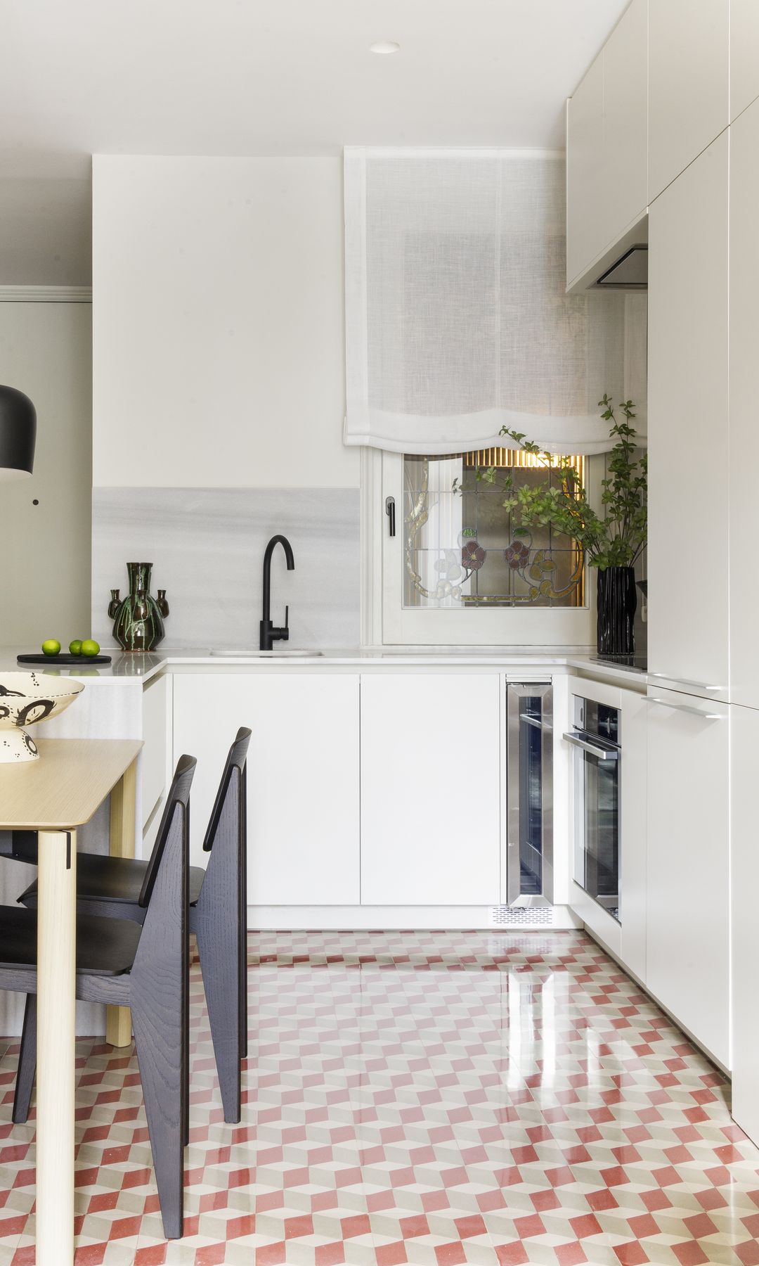 Cocina blanca con el suelo de damero tierra y blanco, mesa de comedor de madera, sillas negras y lámparas de techo negras