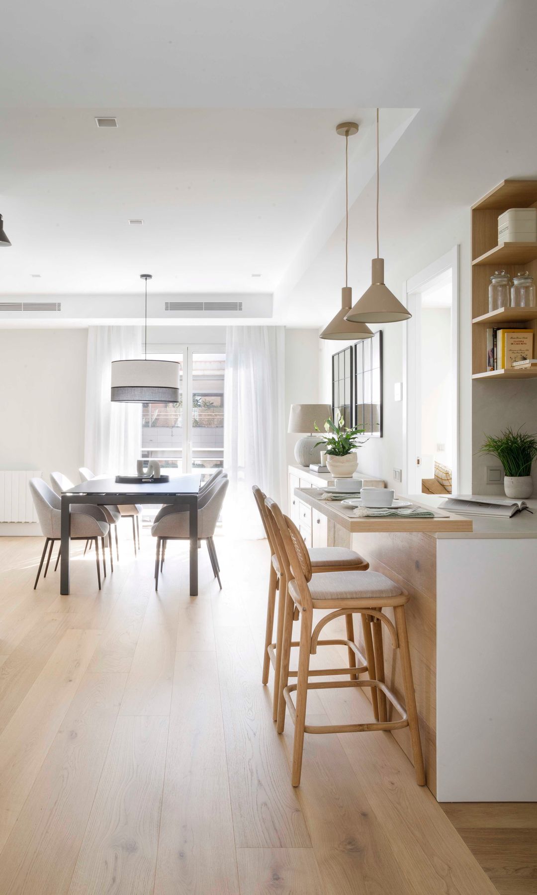 Cocina abierta al comedor, con barra de desayunos con taburetes de madera, baldas de madera, lámparas de techo