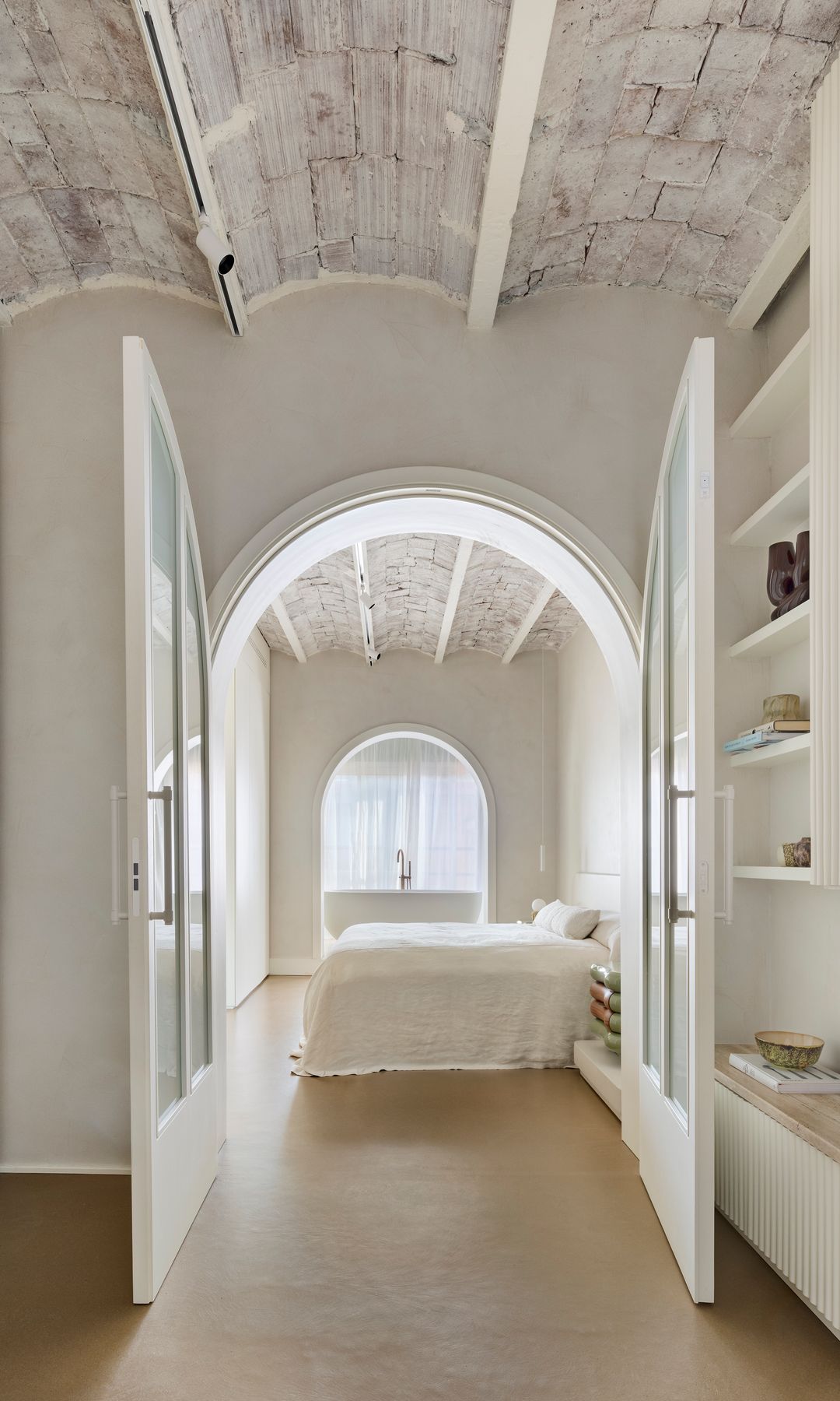 Dormitorio con puerta en forma de arco y bañera exenta, bóvedas catalanas puntadas de blanco, librería acanalada blanca