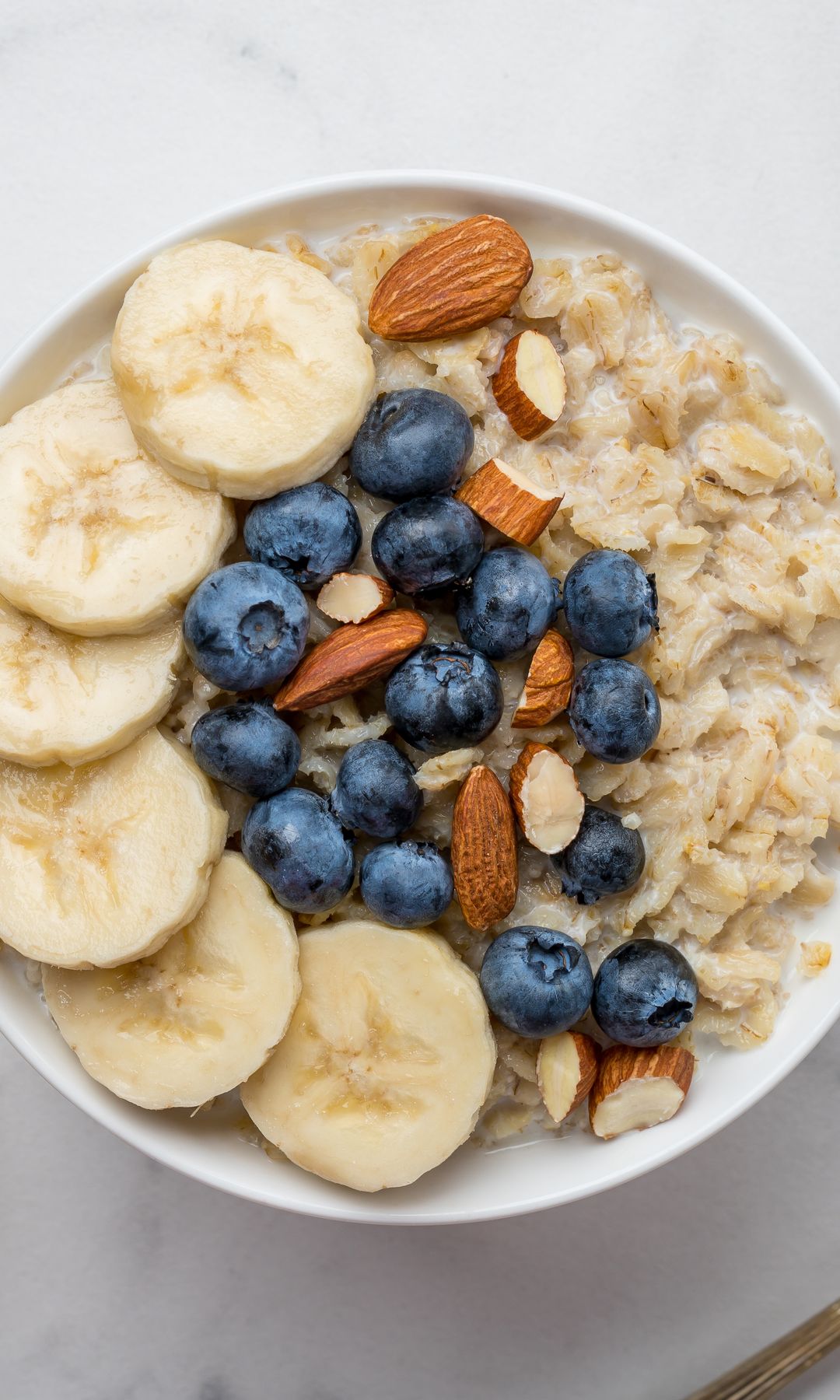 Tazón de avena con plátanos y arándanos, acompañado de cuencos de avena y arándanos.