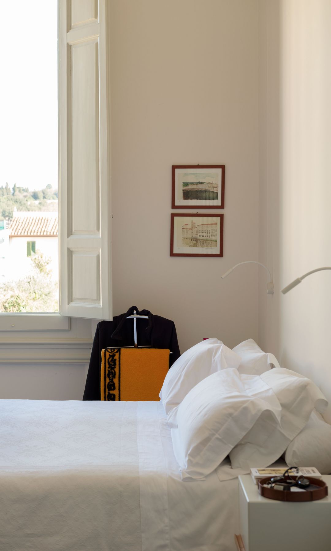 Dormitorio blanco, sin cabecero, ventanas y contraventanas de madera blanca, galán de noche, cuadros en la pared, apliques de pared, ropa de cama blanca