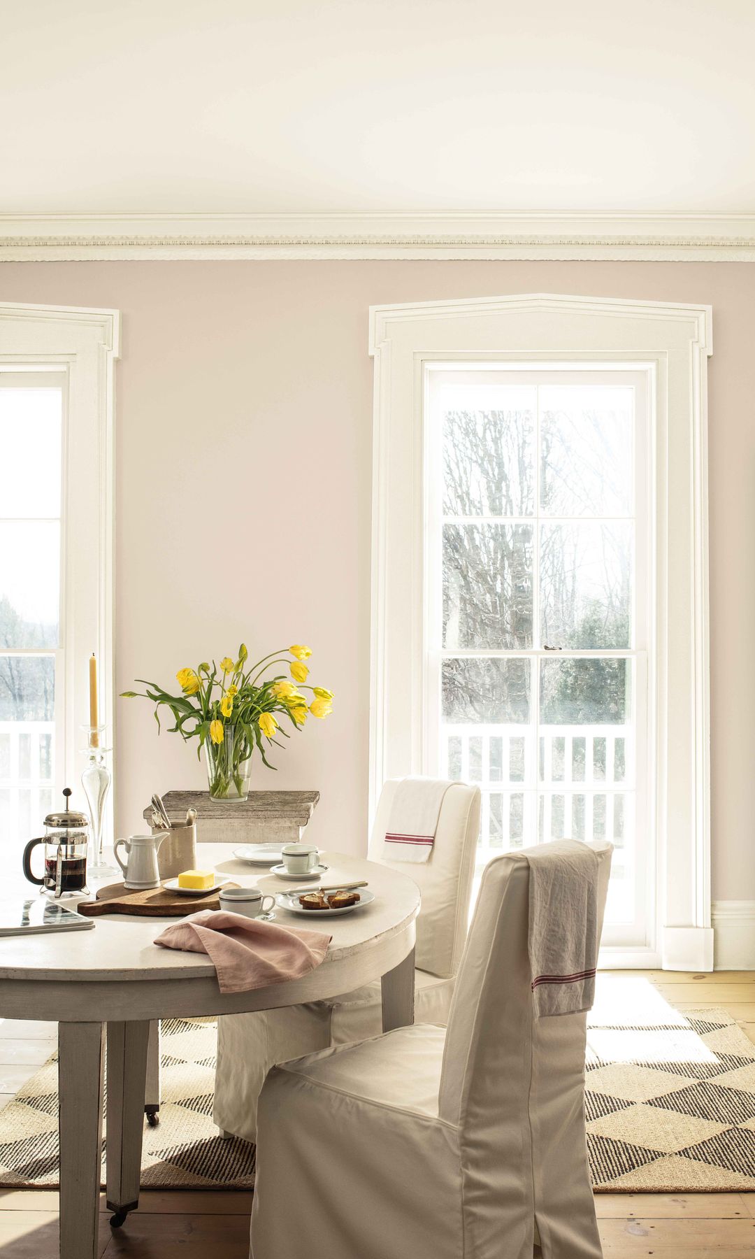 Comedor con sillas con funda blanca, paredes crema, moldura, alfombra., ramo de tulipanes amarillos, salidas exterior