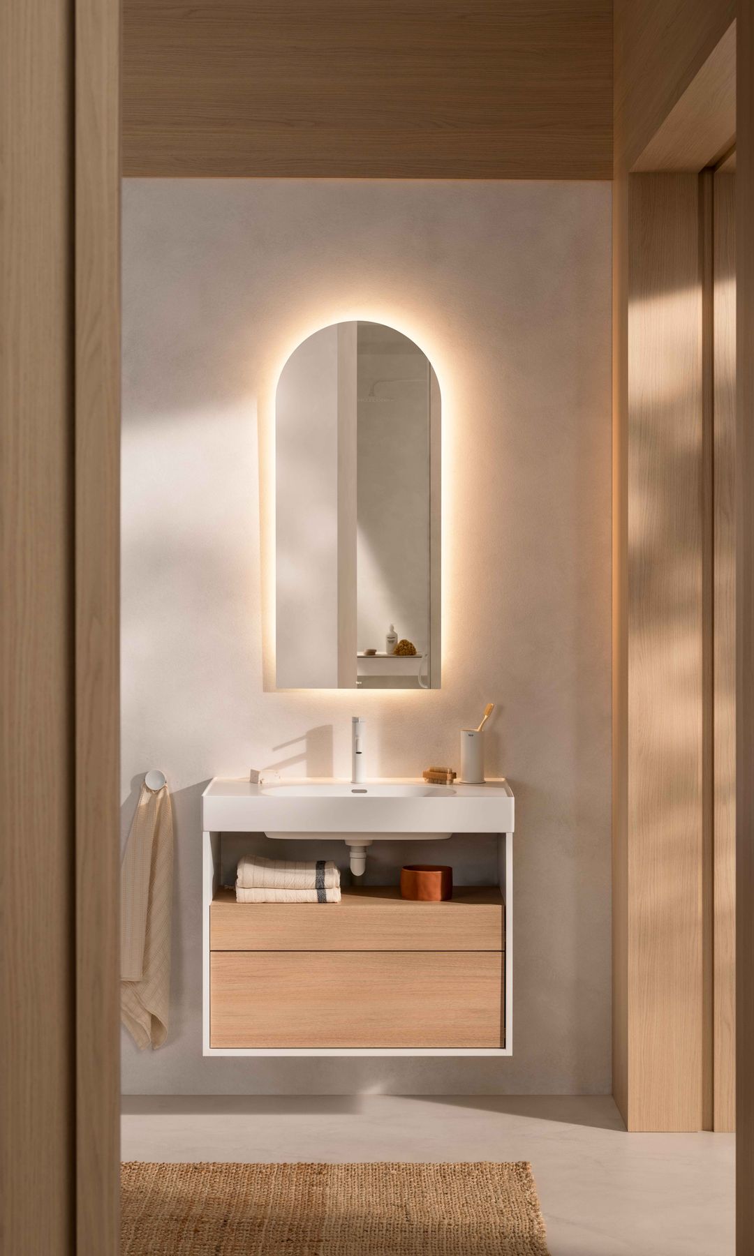 Baño en madera con espejo ovalado retroiluminado, mueble de lavabo volado, alfombra de fibras vegetales 