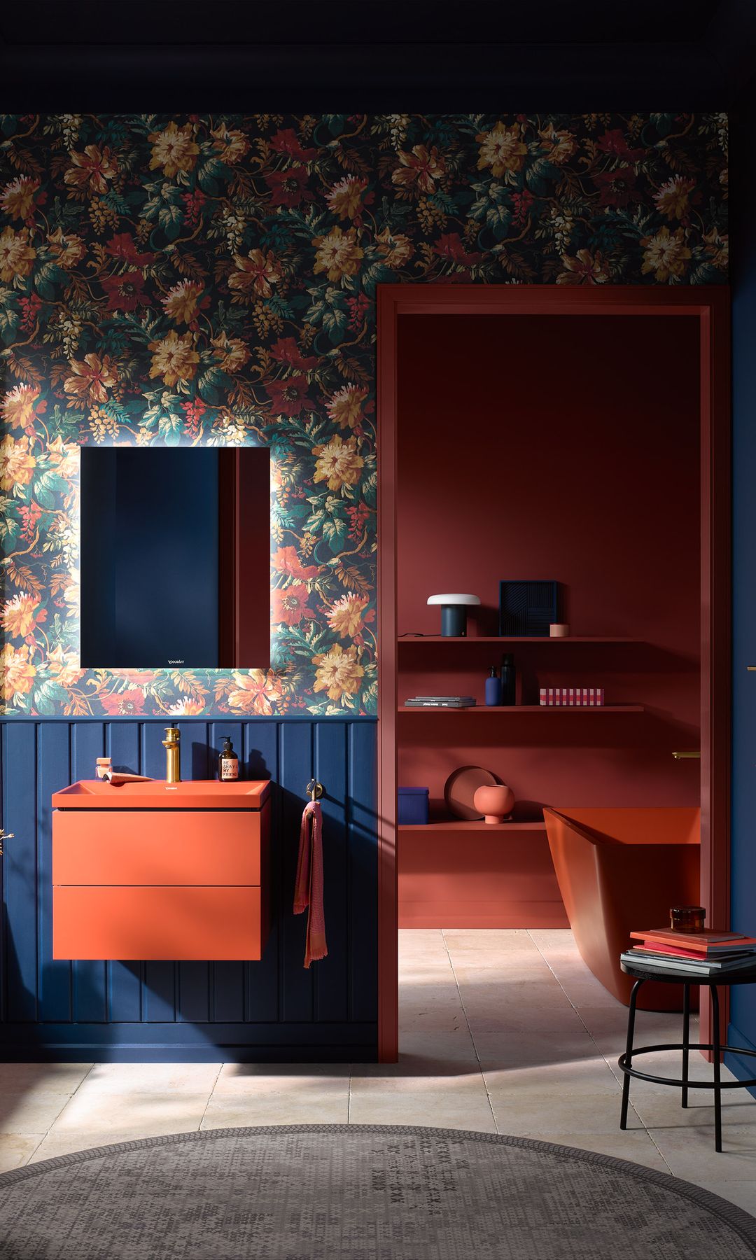 Baño con zócalo alto de madera pintada, paredes azules oscuras, lavabo rojo, papel pintado de flores grandes, alfombra