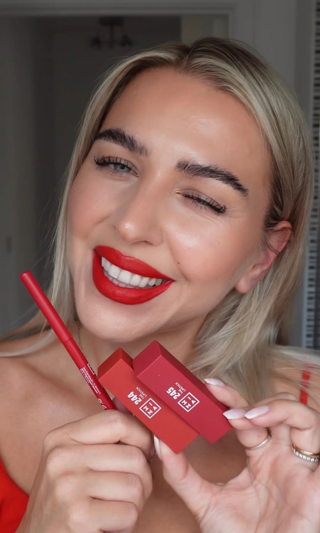 Mujer con labial rojo intenso de subtono frío mostrando un pintalabios y perfilador de labios de 3INA