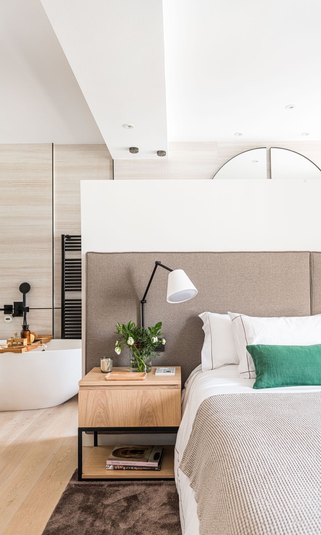 Dormitorio abierto al baño, con cabecero alto entelado, mesita de noche de madera, velas, ramos de flores, aplique