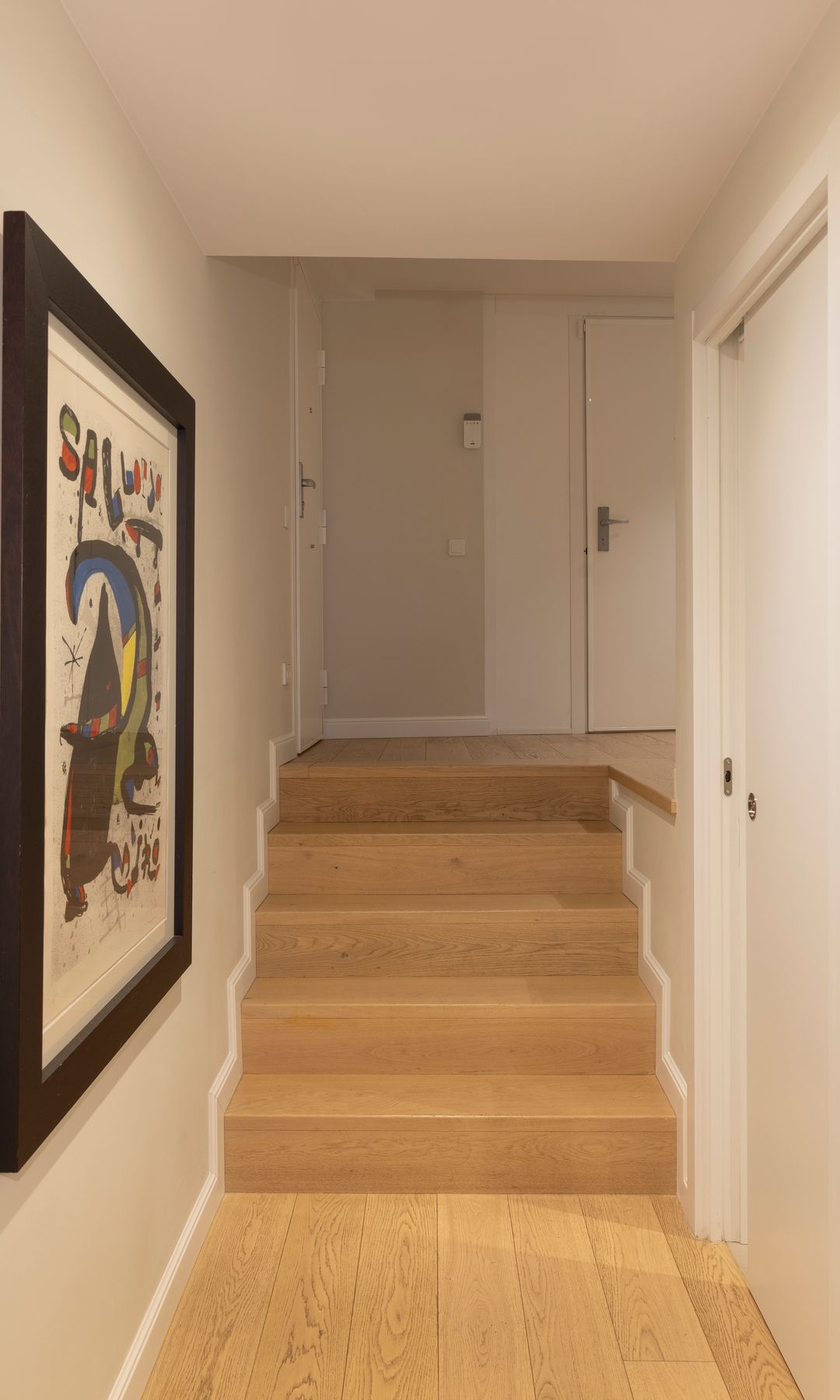 Pasillo con escalera con peldaños de madera, cuadro en la pared y puerta de entrada