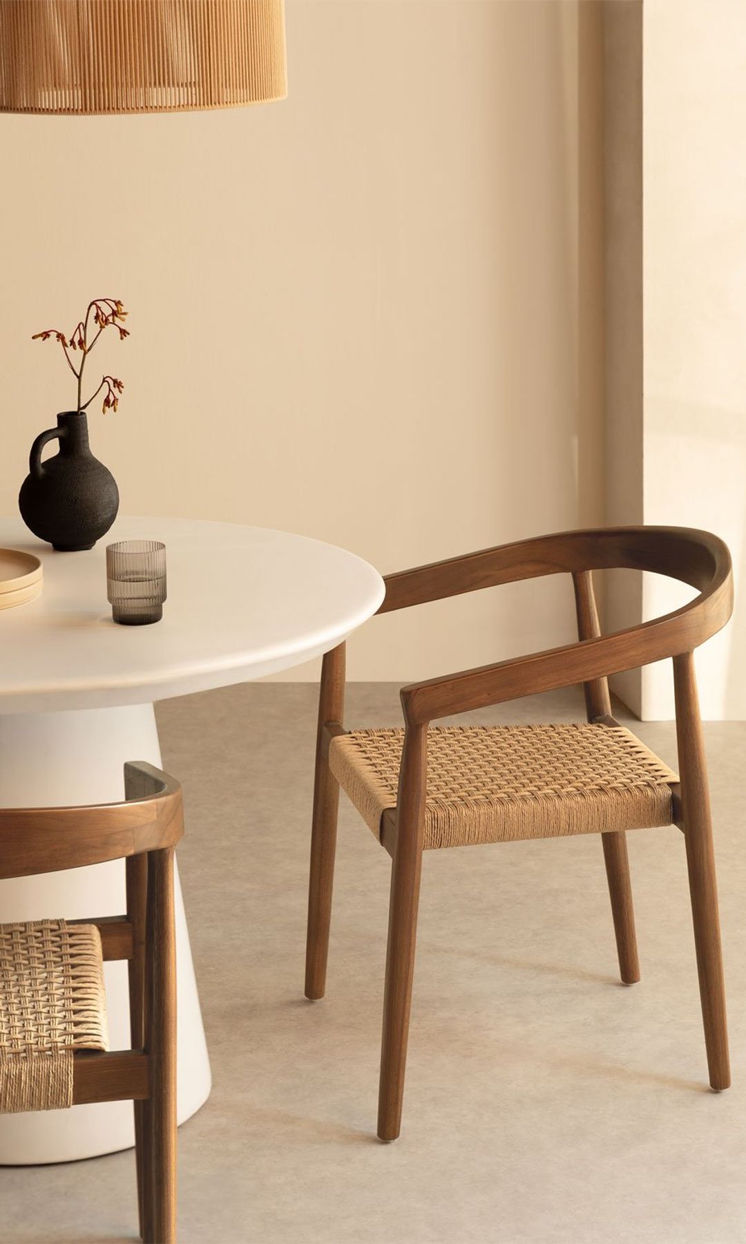Comedor con mesa redonda blanca, sillas de madera con el asiento de cuerda, jarrón y lámpara de fibras vegetales
