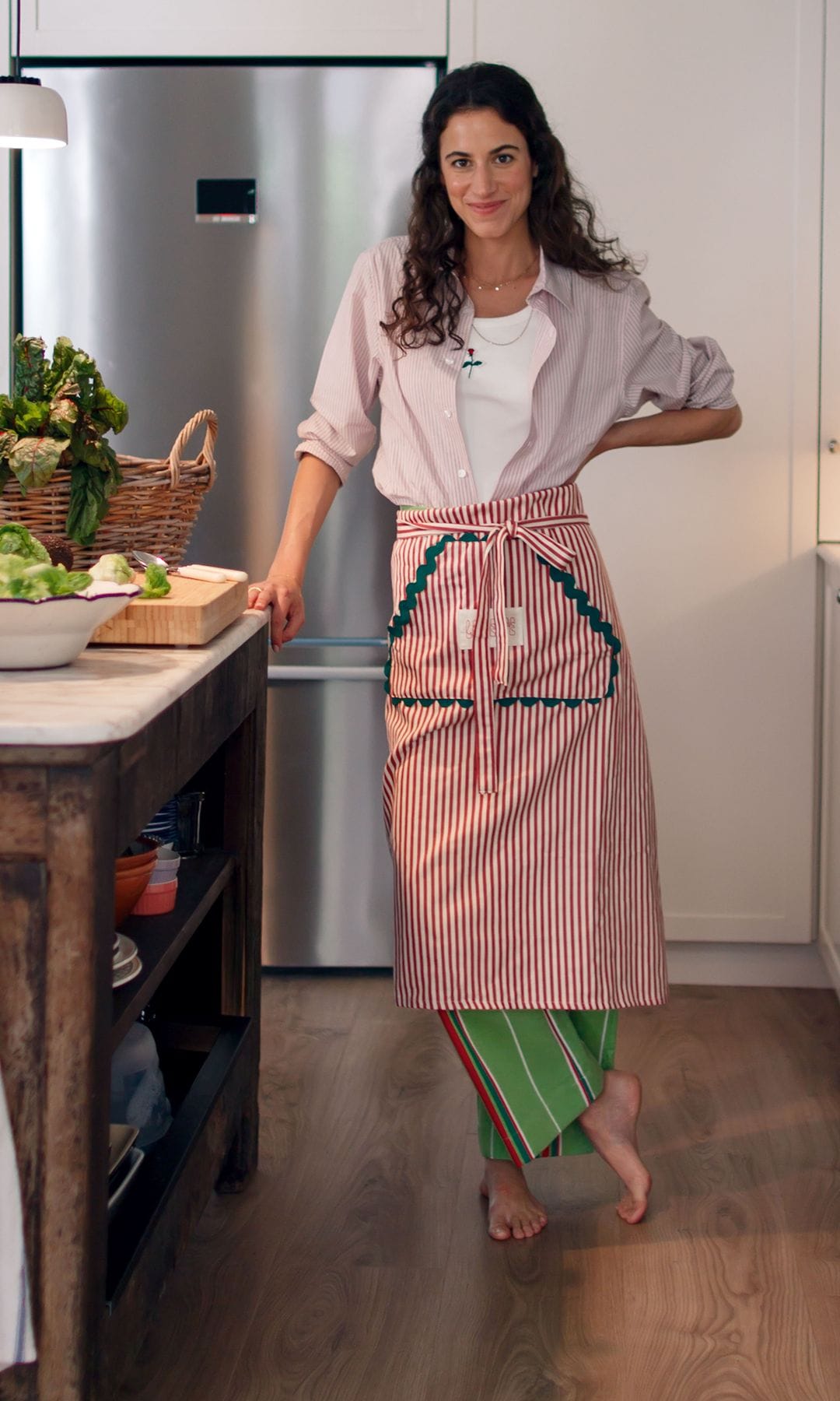 BUENA MANO
Nuestra protagonista, con el delantal puesto, preparando una ensalada en la cocina, coronada por una isla "vintage" de madera envejecida y un tablero de mármol a juego con las encimeras