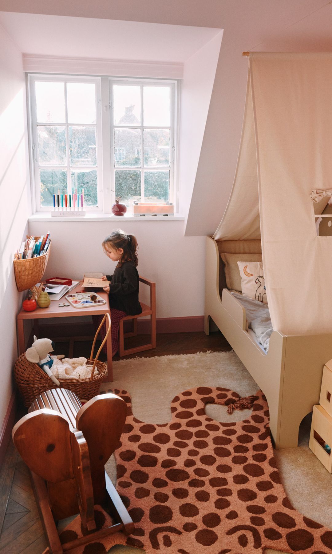 Habitación infantil con niña pintando en una mesita baja, alfombra de animal, cama tipo casita y elefante de madera 