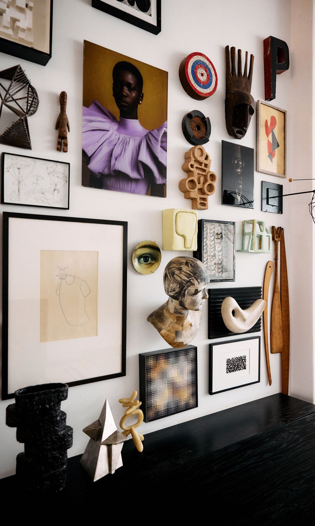 Rincón con aparador negro y pared con fotos láminas, cuadros, máscaras y objetos 