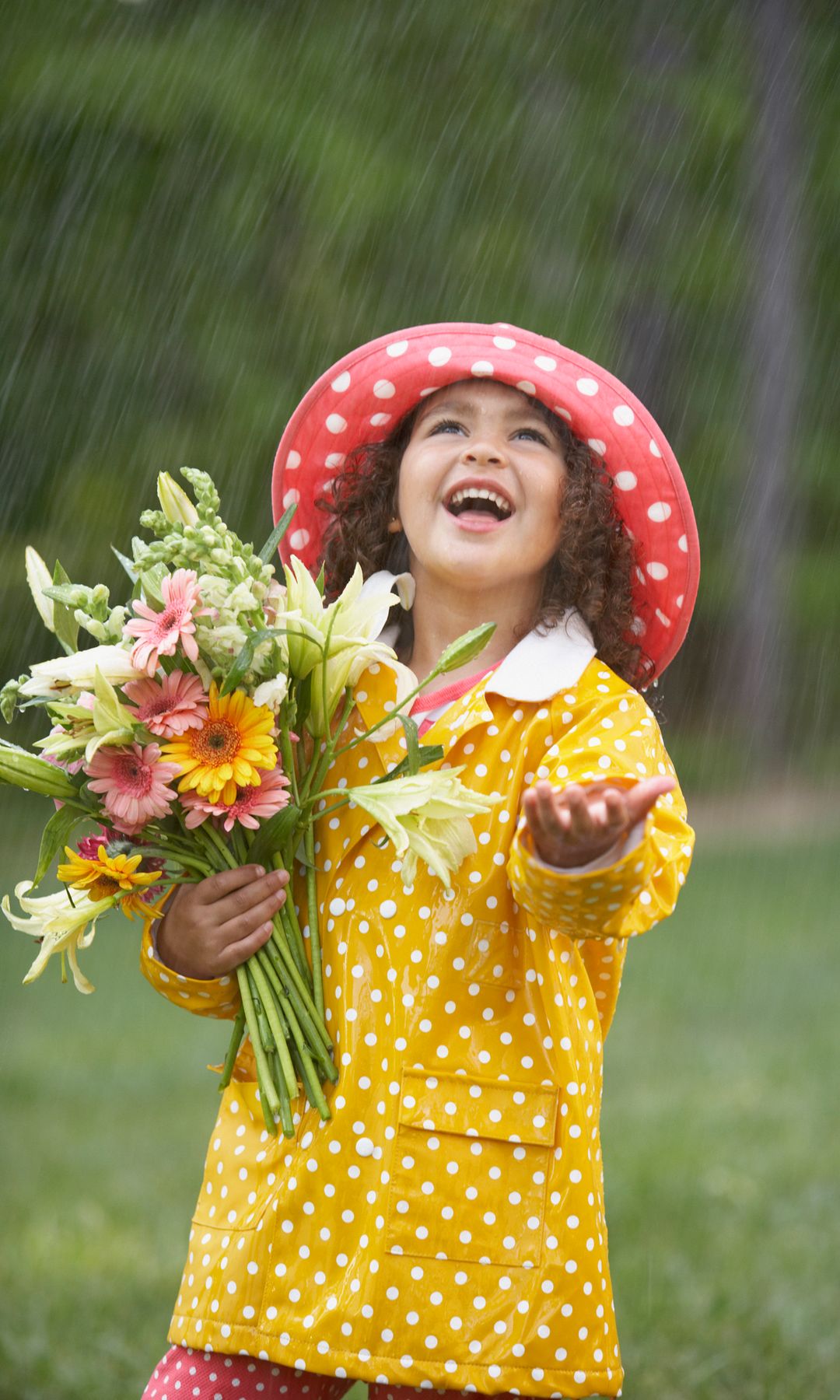 Niña con flores y gabardina sonríe bajo la lluvia en primavera