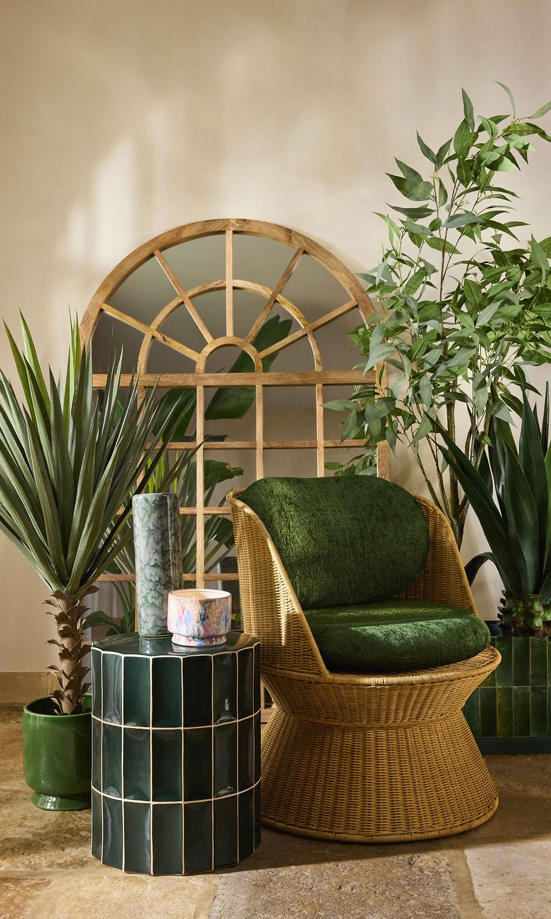 Rincón casa con plantas, espejo ovalado con cuarterones, butaca de mimbre, mesa auxiliar de azulejos verdes