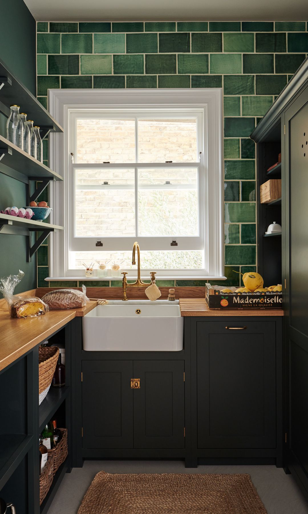 Cocina estrecha con azulejos verdes de dos tonos, muebles verde oscuro, ventana, alfombra de fibras vegetales