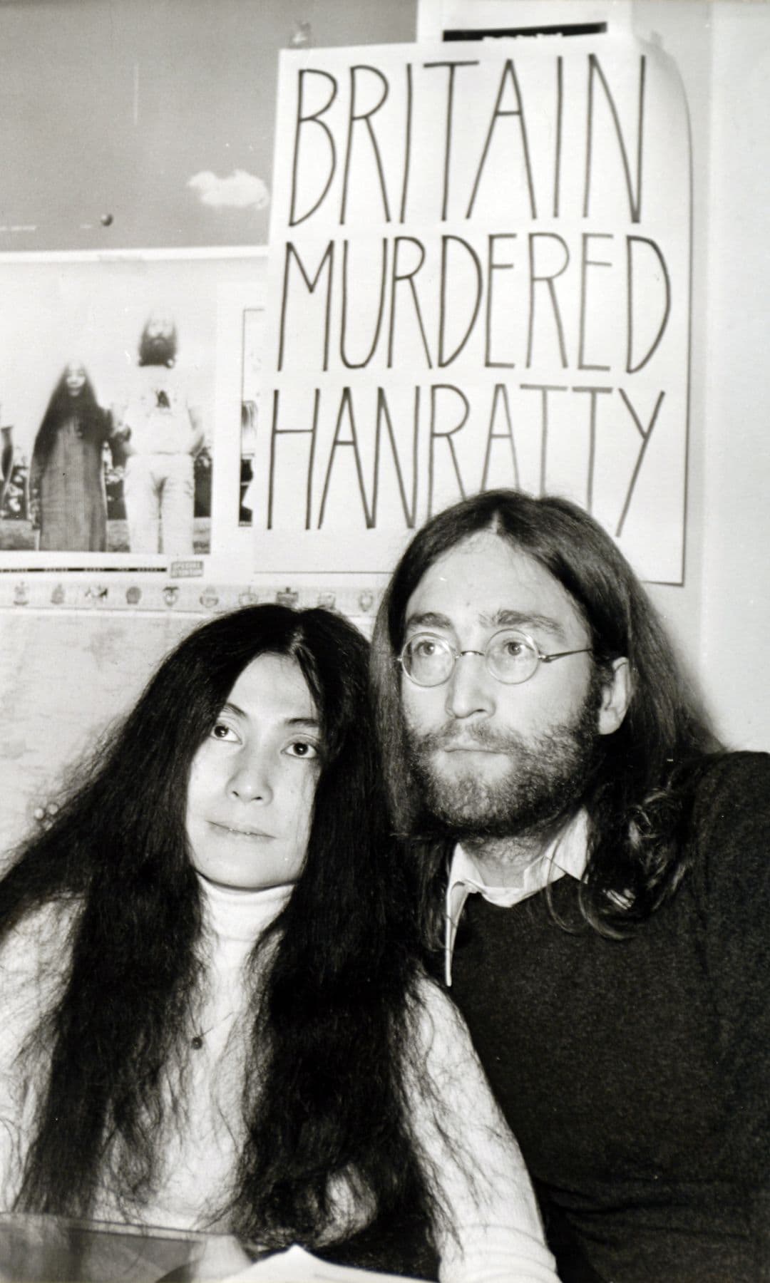Yoko Ono y John Lennon sentados juntos, con cartel 'BRITAIN MURDERED HANRATY' detrás.