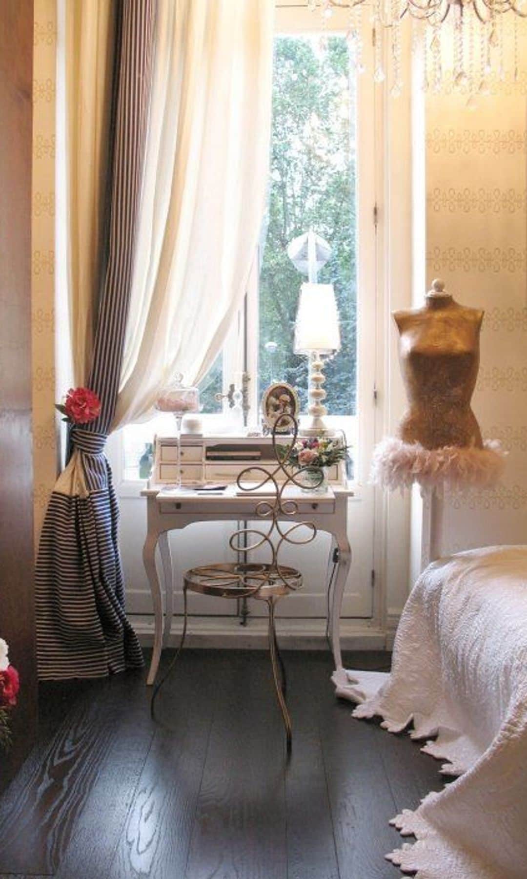 Tocador con mesa antigua, maniquí, jarrón con flores, cortinas blancas, lámpara de techo, lámpara de sobremesa, suelo de madera oscura