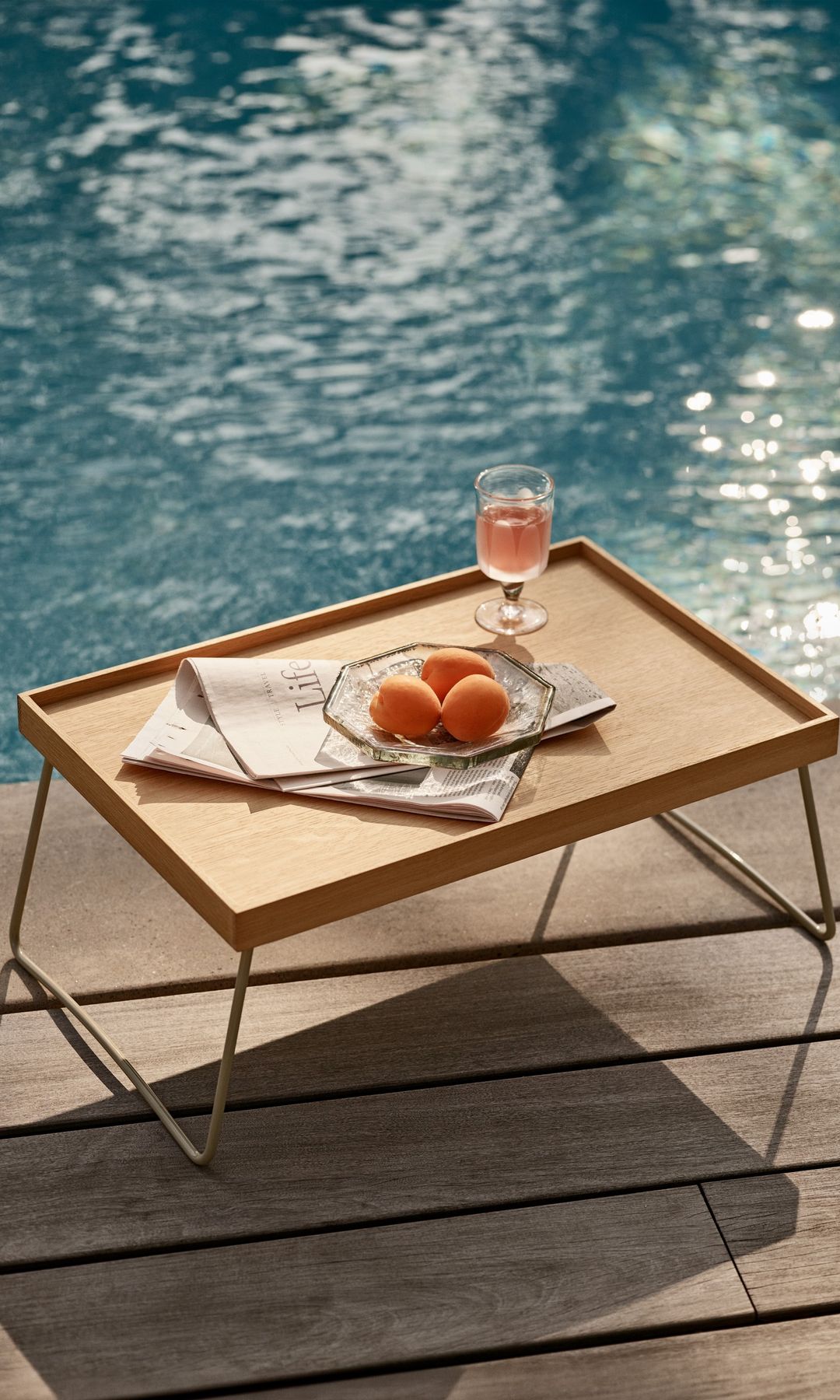 Mesa auxiliar de madera al borde de la piscina con plato y copa