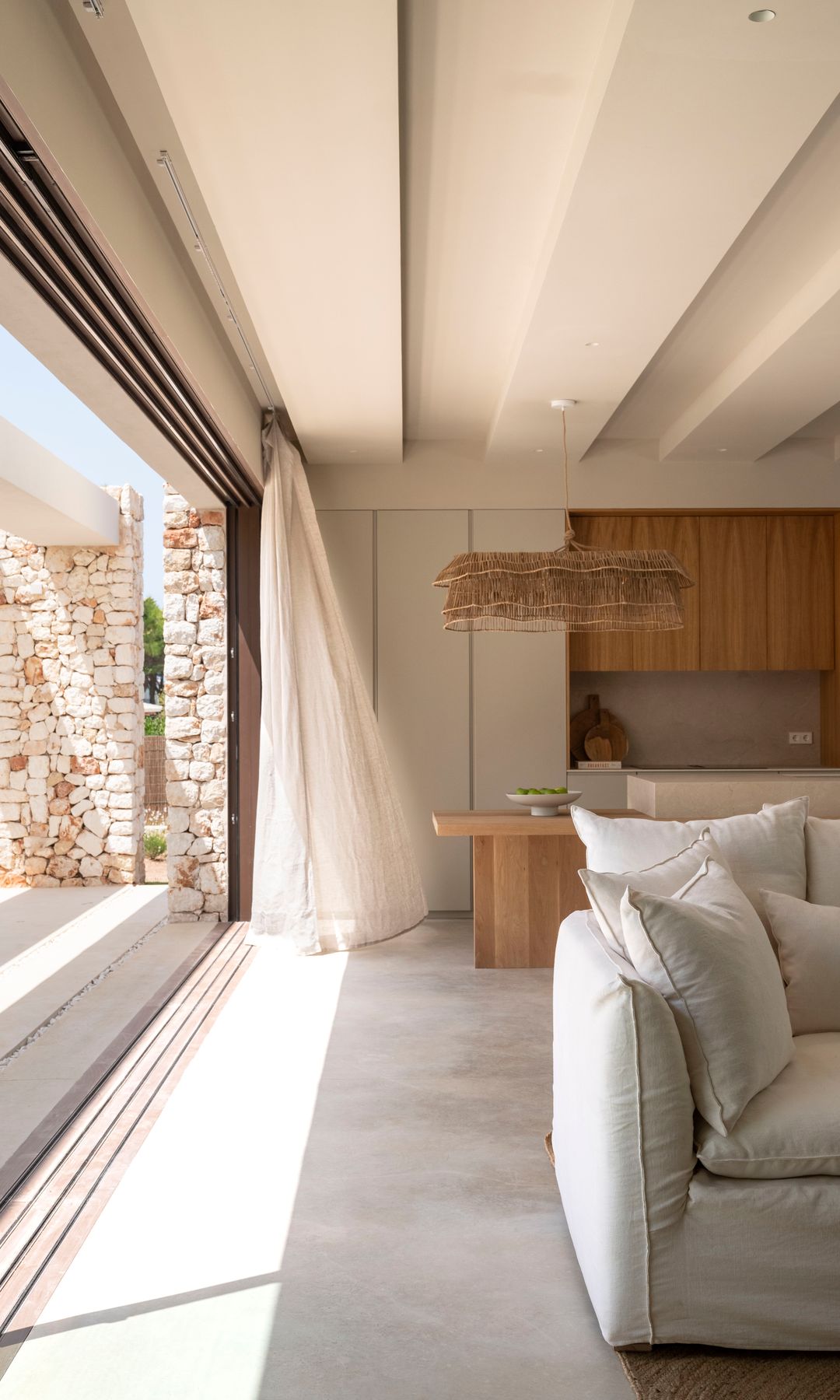 Cocina abierta al salón con cortina de lino beige, mueble de cocina blancos y de madera, lámpara de fibras vegetales 