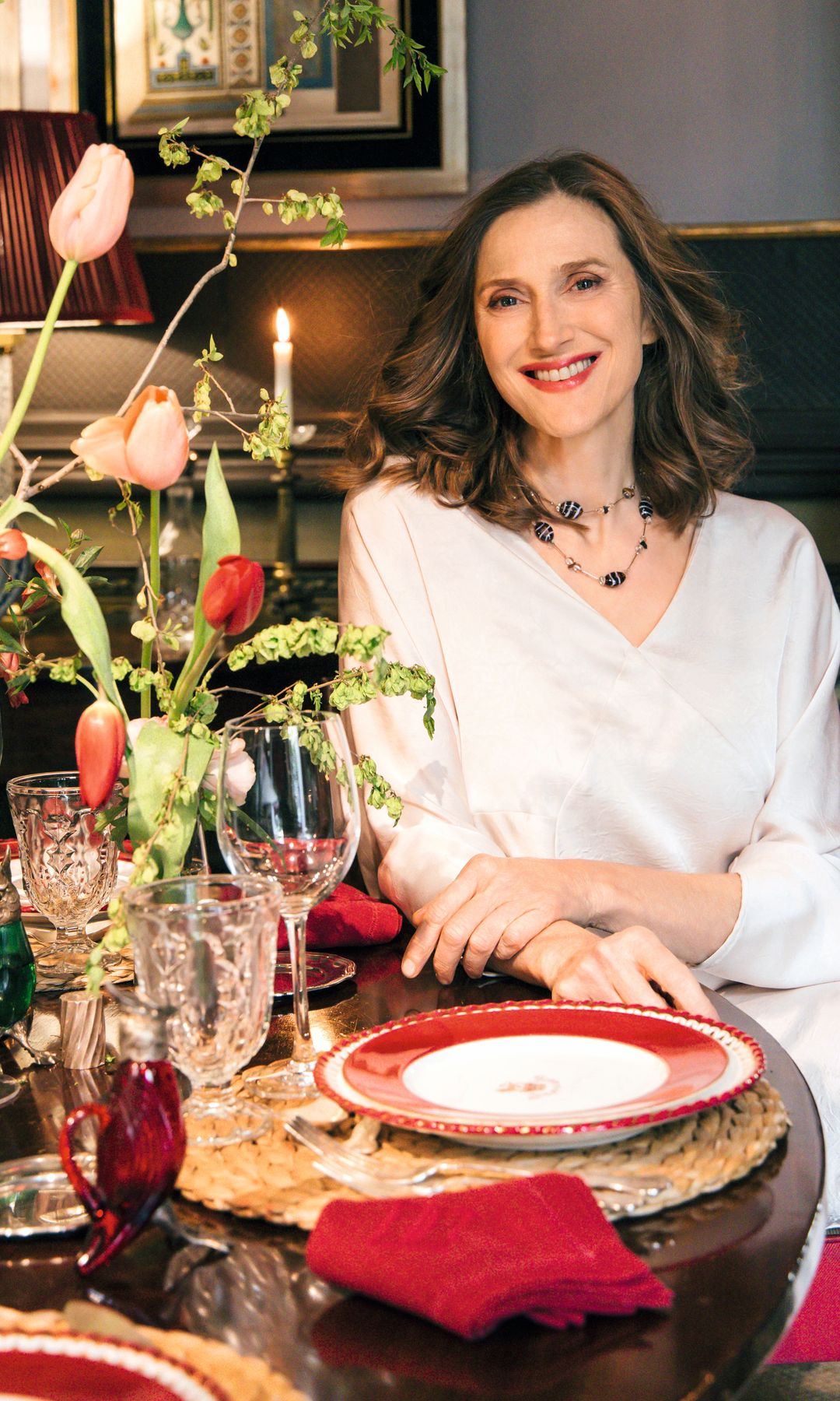 Inés, sentada a la mesa, elegantemente decorada con bajoplatos de vidrio rojo en relieve y una vajilla clásica