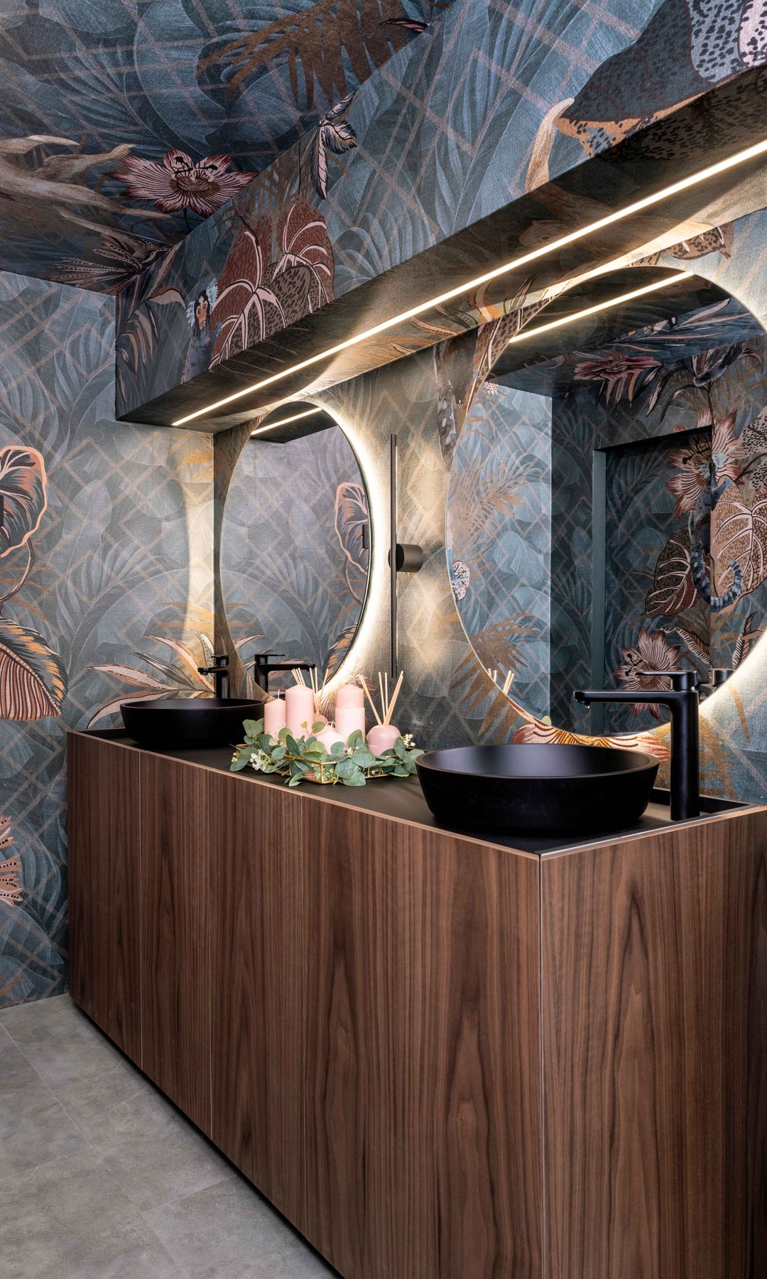 Baño con papel pintado, doble lavabo, espejos redondos retroiluminados y mueble de madera