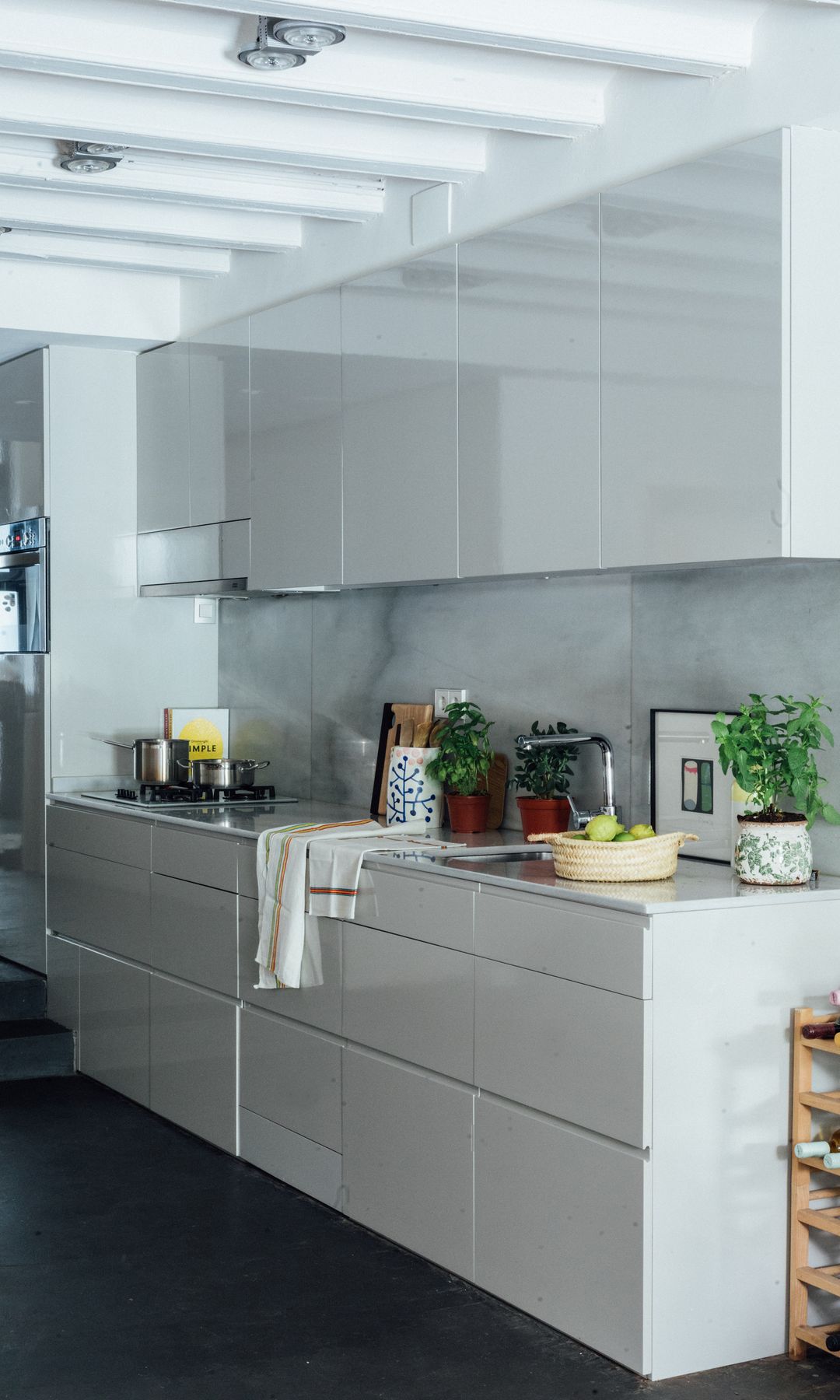 Cocina blanca, suelo negro, muebles de cocina hasta el techo, antepecho de mármol, botellero de madera, plantas
