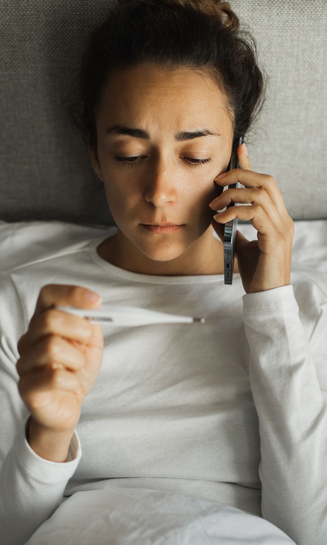 Mujer con un termómetro en la mano llamando por teléfono