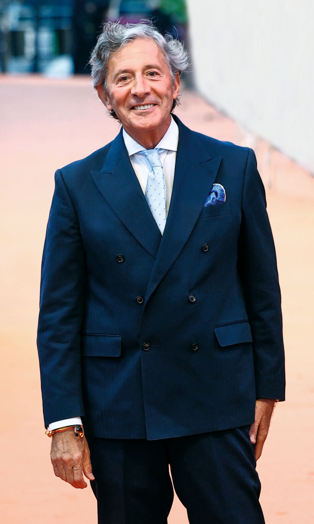 Jesús Álvarez en traje azul, corbata celeste y zapatos negros, sonriendo en un pasillo