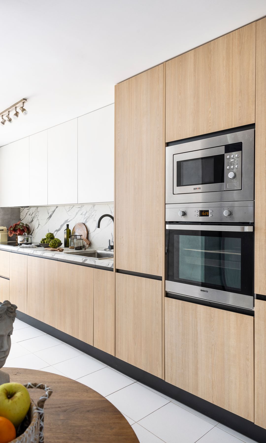 Cocina alargada con muebles de madera, electrodomésticos en columna, focos en el techo