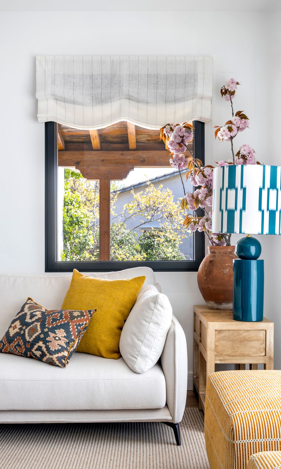 Salón con sofá blanco, ventana con perfiles negros, lámpara de cerámica azul, cojines