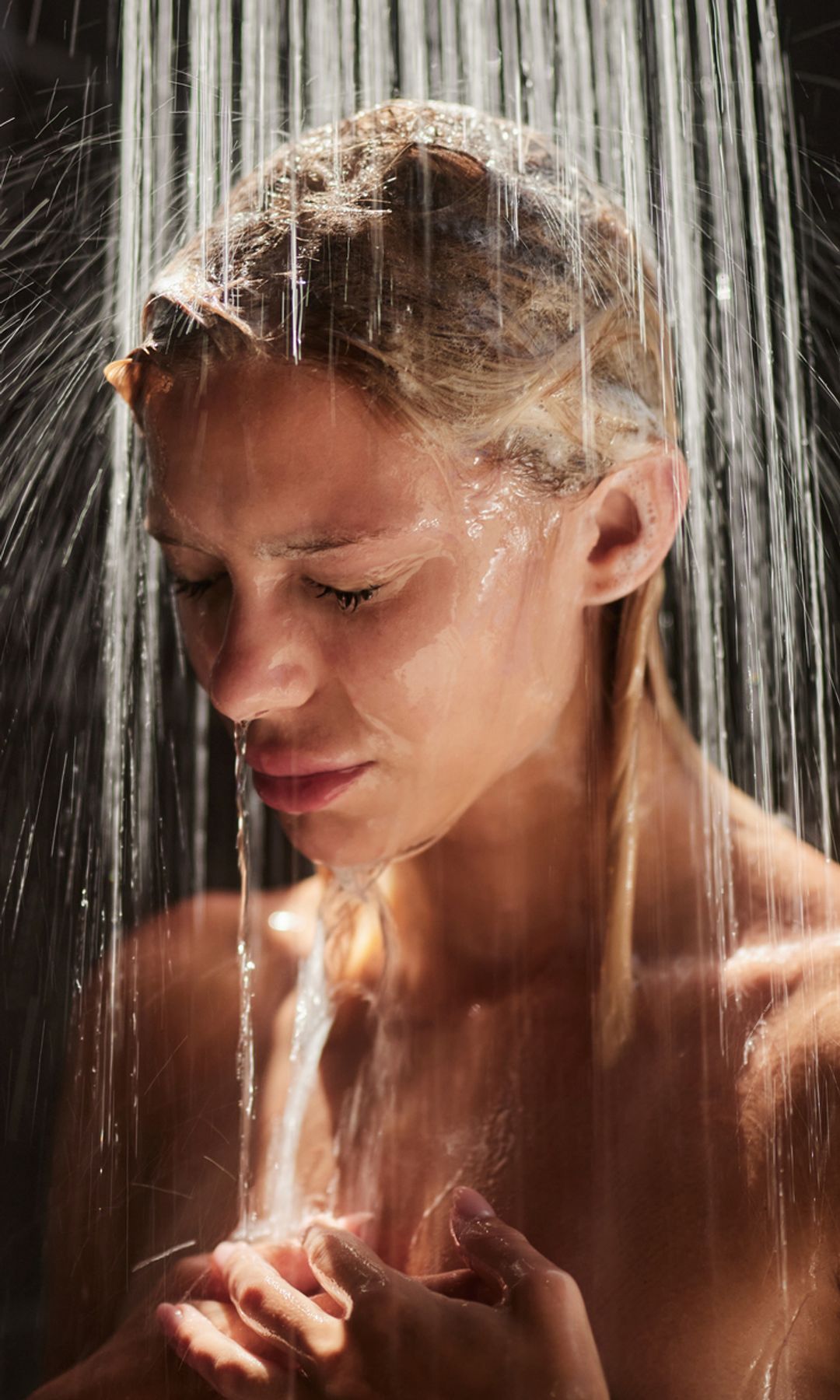 Mujer en la ducha con los ojos cerrados y las manos en el pecho.