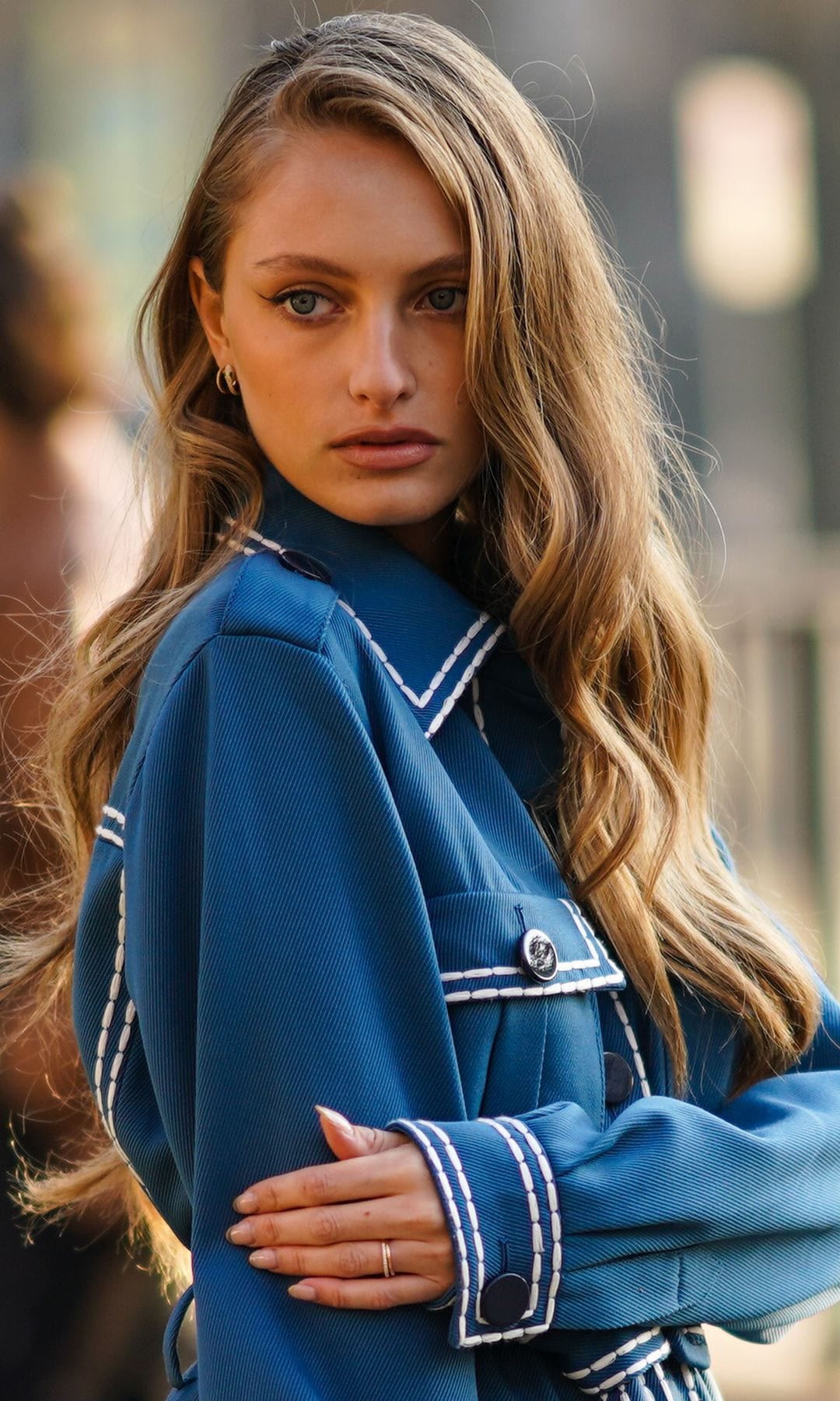 MILAN, ITALY - JANUARY 13:  A guest wears gold earrings, a long oversized blue and visibly white seams jacket, blue set pants, a black shiny leather Fendi handbag, gold and silver rings, outside Fendi, during Milan Fashion Week Menswear Fall/Winter 2020/2021, on January 13, 2020 in Milan, Italy. (Photo by Edward Berthelot/Getty Images)