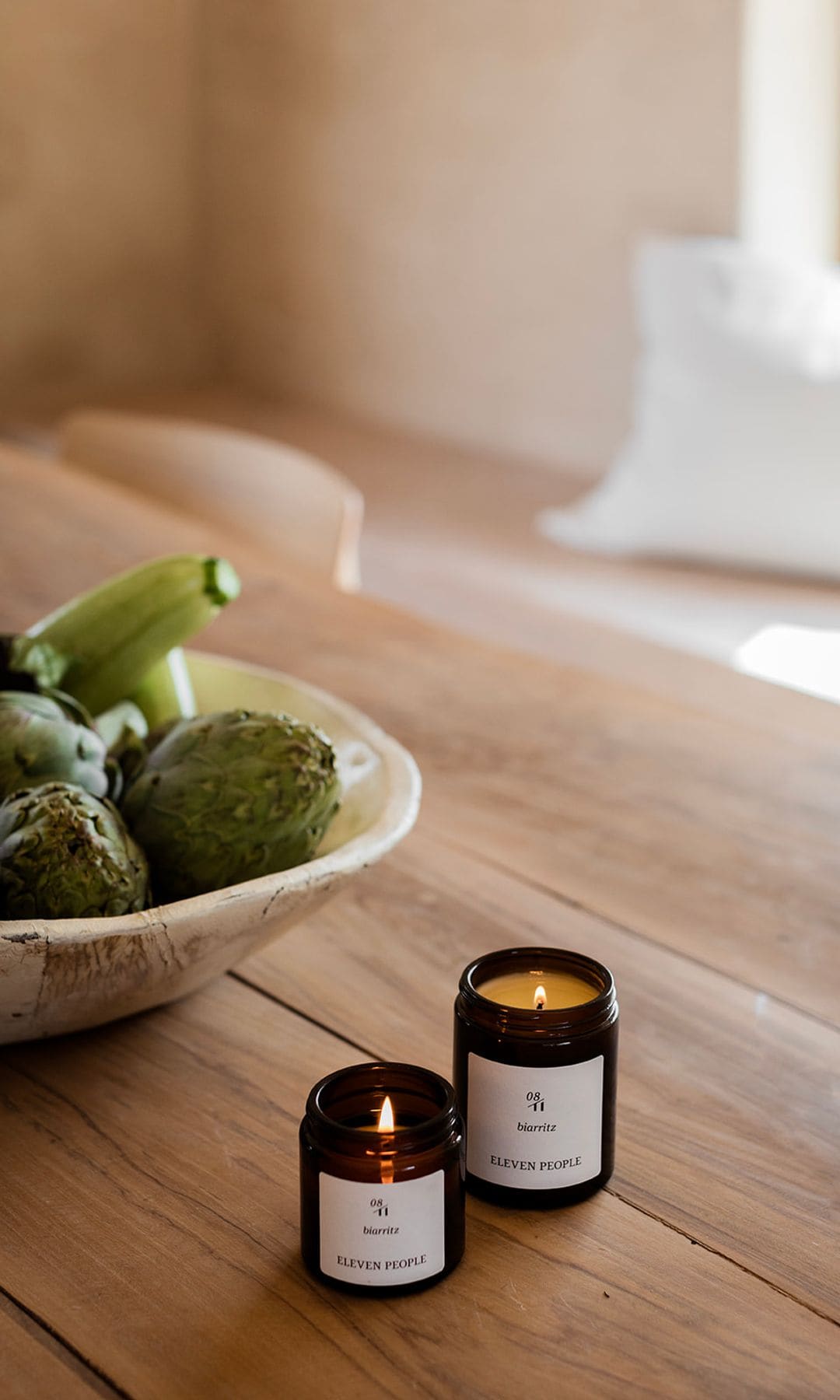Velas de Eleven People sobre mesa de madera, con frutero con alcachofas